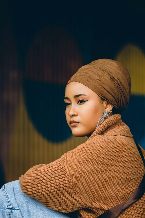 Free Portrait of a young woman in Abuja, Nigeria, wearing a brown turban and sweater, with artistic background. Stock Photo