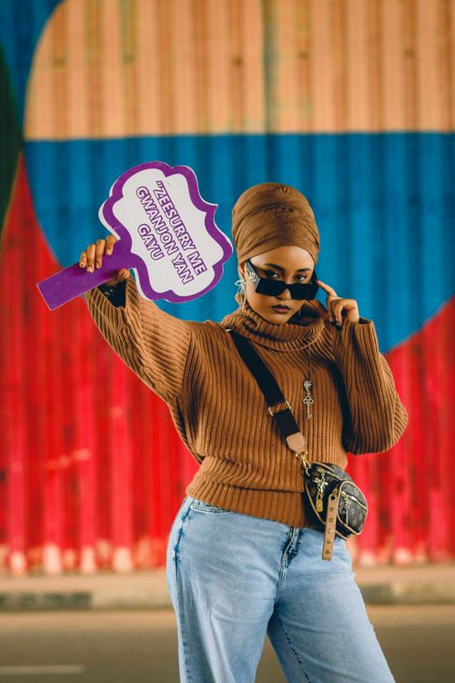 Free Fashionable woman in sunglasses poses with sign against colorful background in Abuja, Nigeria. Stock Photo