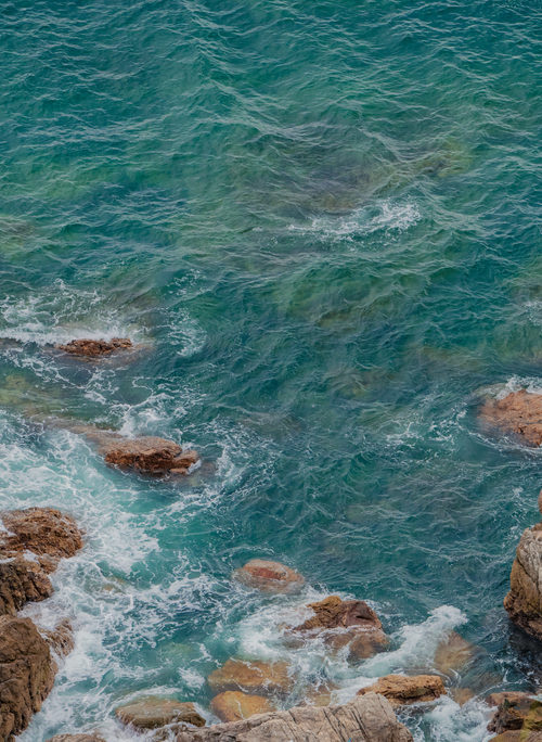 Free Aerial shot of clear turquoise ocean waves crashing against rocky coast. Stock Photo