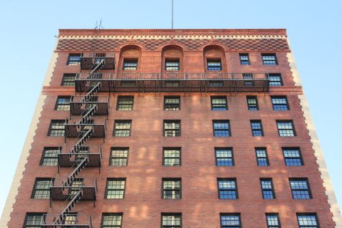 Free Front view of a classic brick building featuring a metal fire escape under clear blue sky. Stock Photo