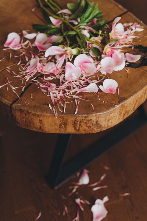 Free Pink rose petals scattered on a rustic wooden table create an artistic, romantic scene. Stock Photo