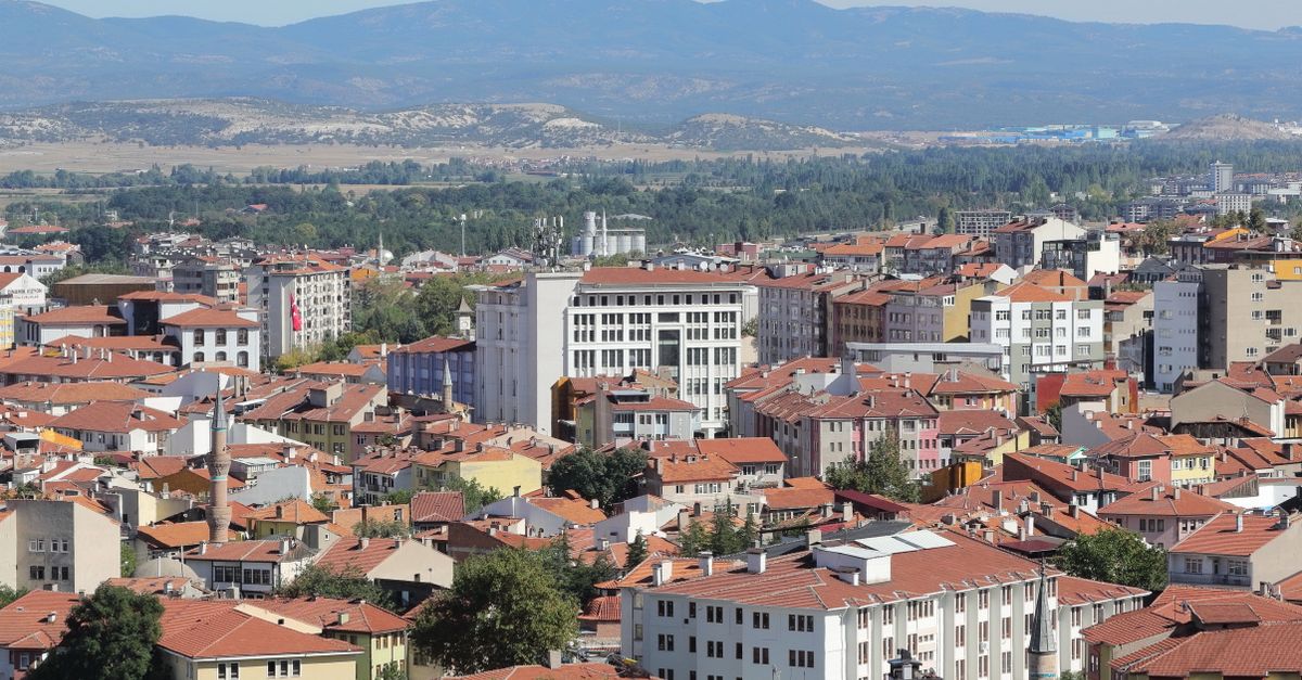 Panoramic view of a city's red rooftops with mountains in the background, captured during the day.