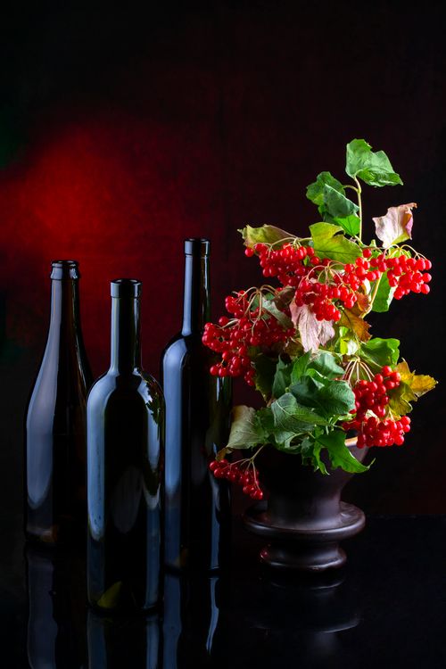 Free Sophisticated still life featuring dark wine bottles and vibrant berries against a rich background. Stock Photo