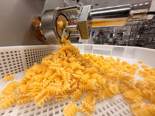 Free Close-up of fresh pasta being extruded in a modern factory setting. Stock Photo
