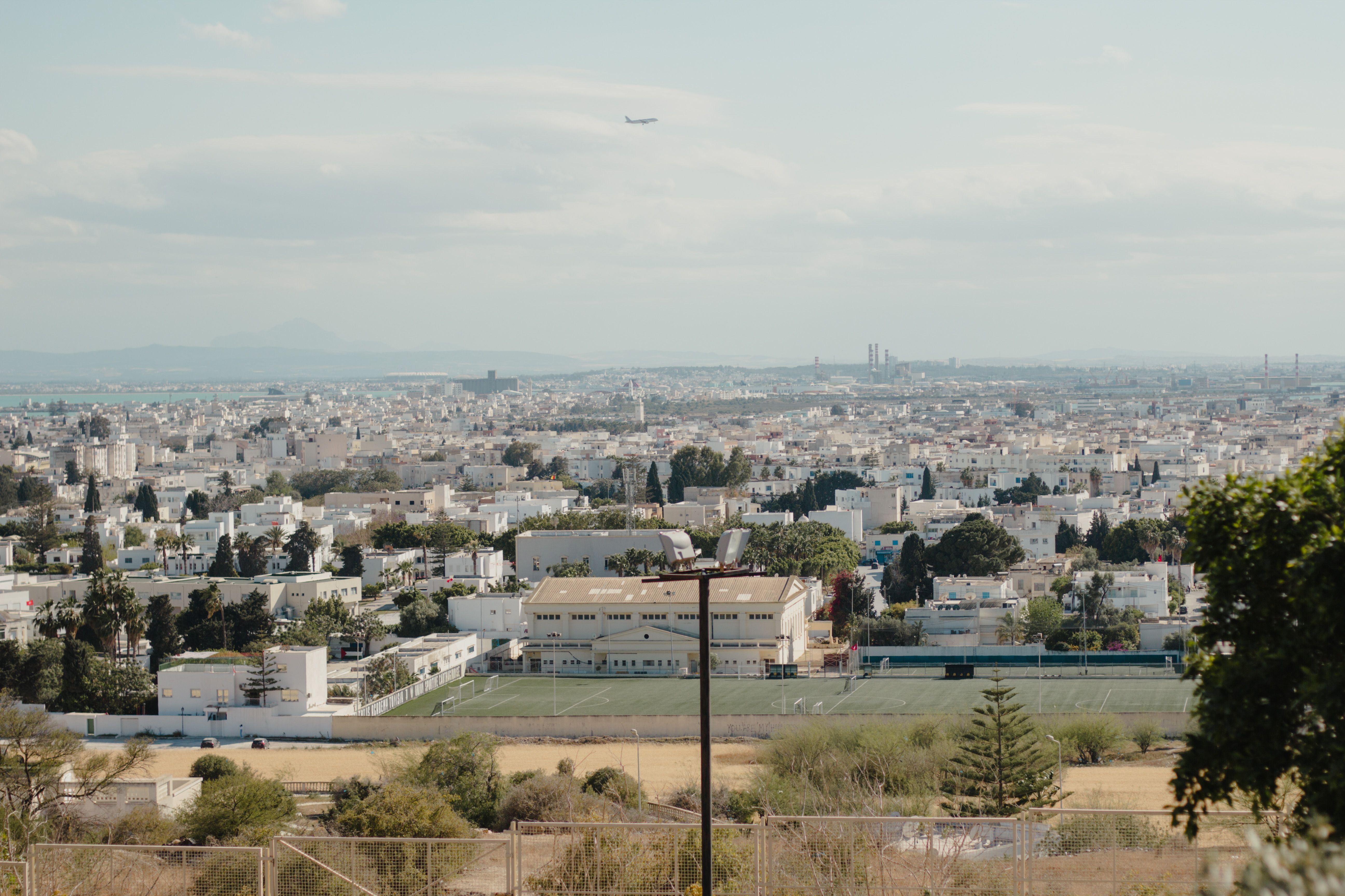 Aerial cityscape of Tunis with a plane in the sky, featuring urban buildings and greenery. — lounges at Tunis Airport