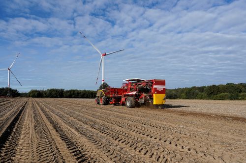 Free Efficient potato harvesting with machinery near wind turbines in Lütau, Germany. Stock Photo