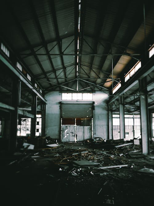 Huge hall of empty abandoned industrial building including trash on floor and high grey ceiling supported by columns