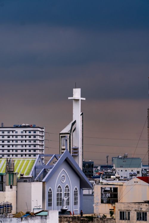 Free A cityscape featuring a church with a white cross under a moody sunset sky. Stock Photo