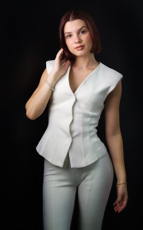 Free Portrait of an elegant woman in a chic white outfit against a dark background, exuding style and confidence. Stock Photo