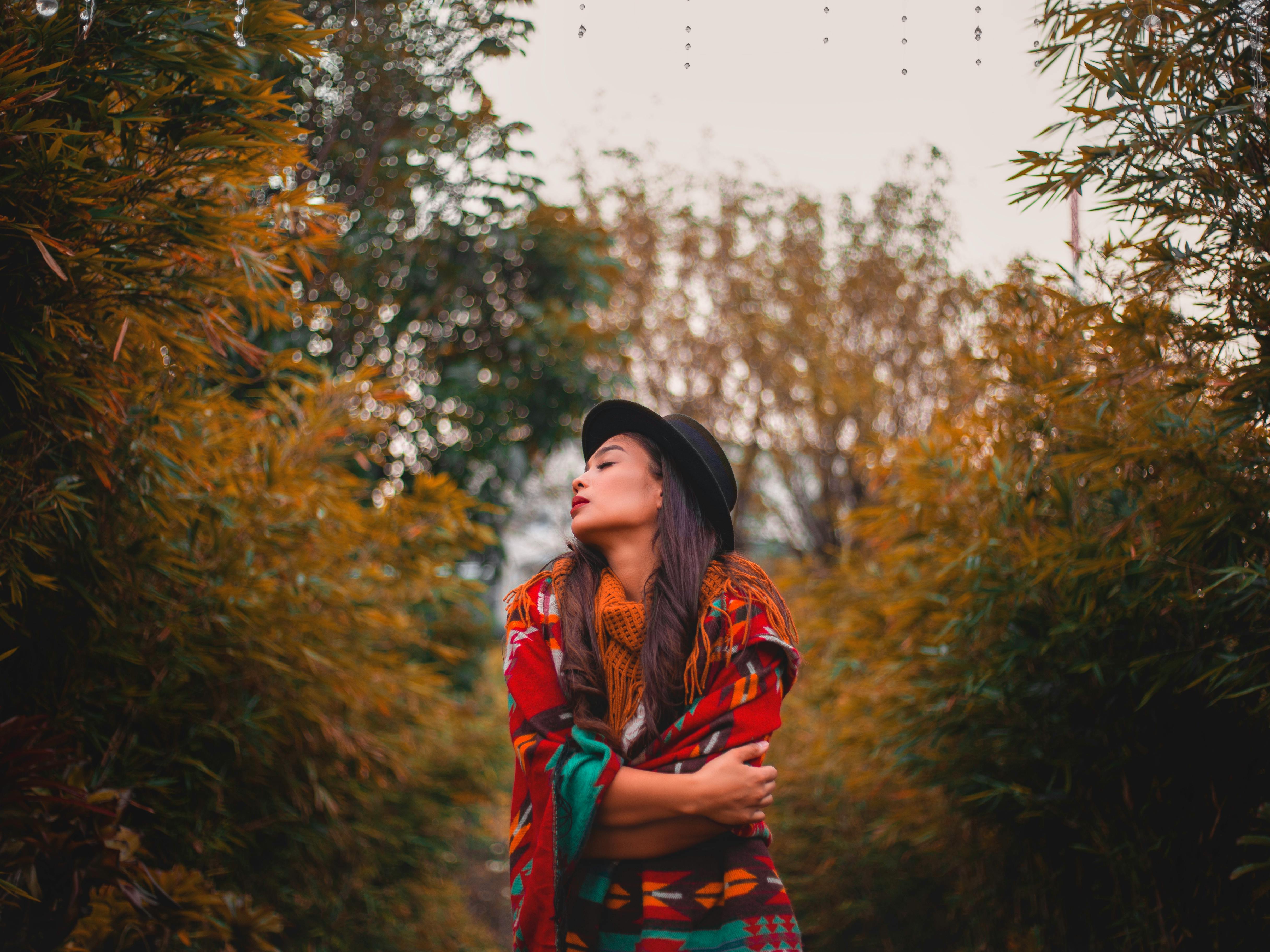在郁郁葱葱的秋季公园里，一名女子裹着彩色毯子，享受宁静的时刻