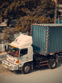 A large container truck parked on a city road, surrounded by trees during daytime.