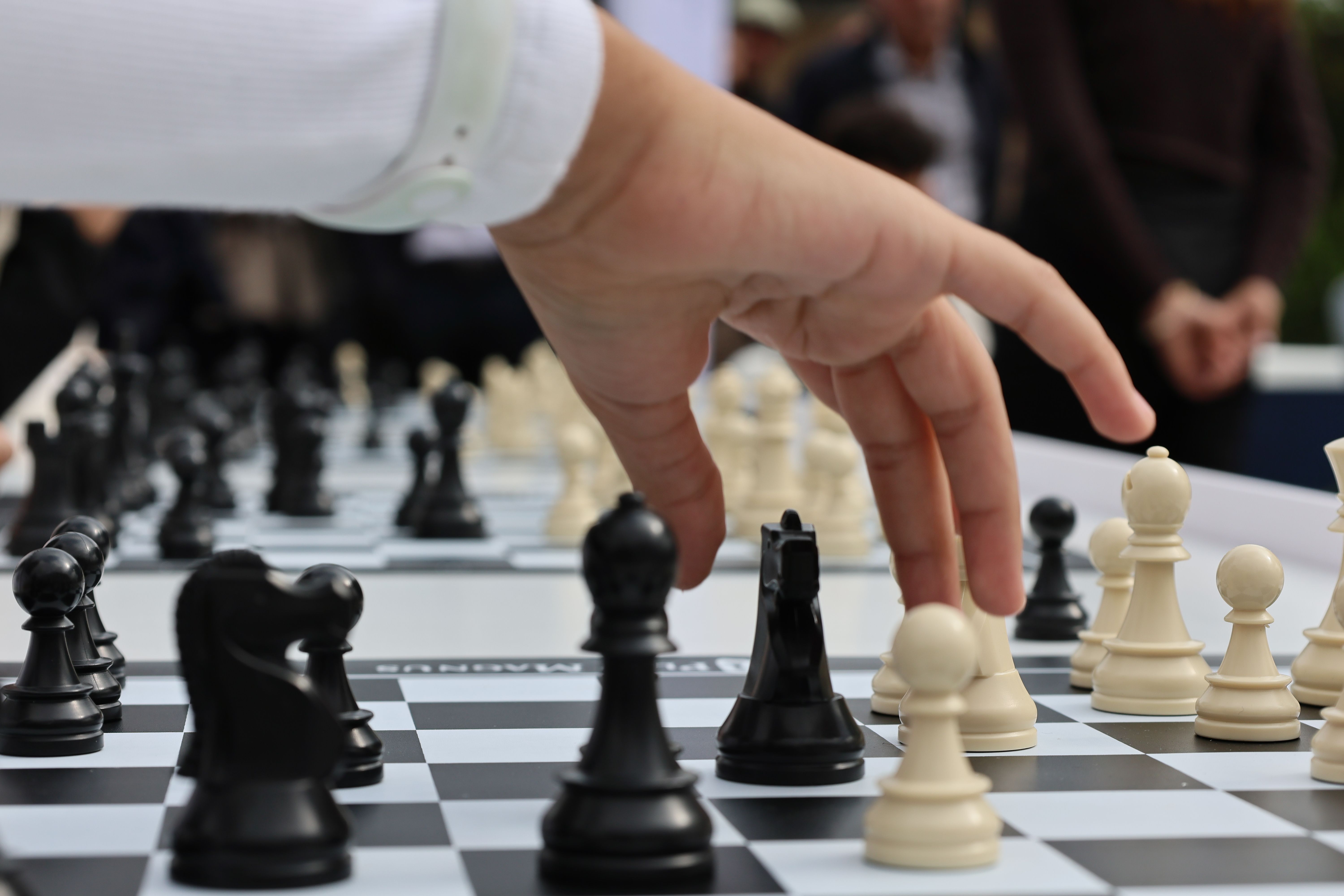Hand moves a pawn on a chessboard, focusing on strategy and competition.