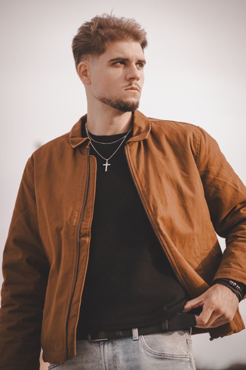 Free Portrait of a fashionable man in a brown jacket standing outdoors, exuding confidence and style. Stock Photo