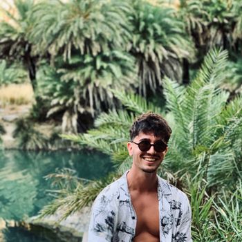 A joyful man in sunglasses enjoys a tropical oasis in Rethimno, Greece, surrounded by lush palms.