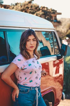 Chic woman leaning on vintage van in sunny countryside, capturing a carefree summer vibe.