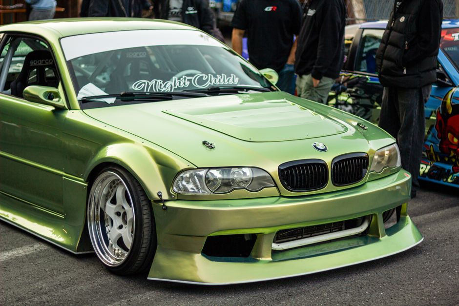A sleek, customized green sports car showcased at an outdoor street car show with a vibrant crowd.