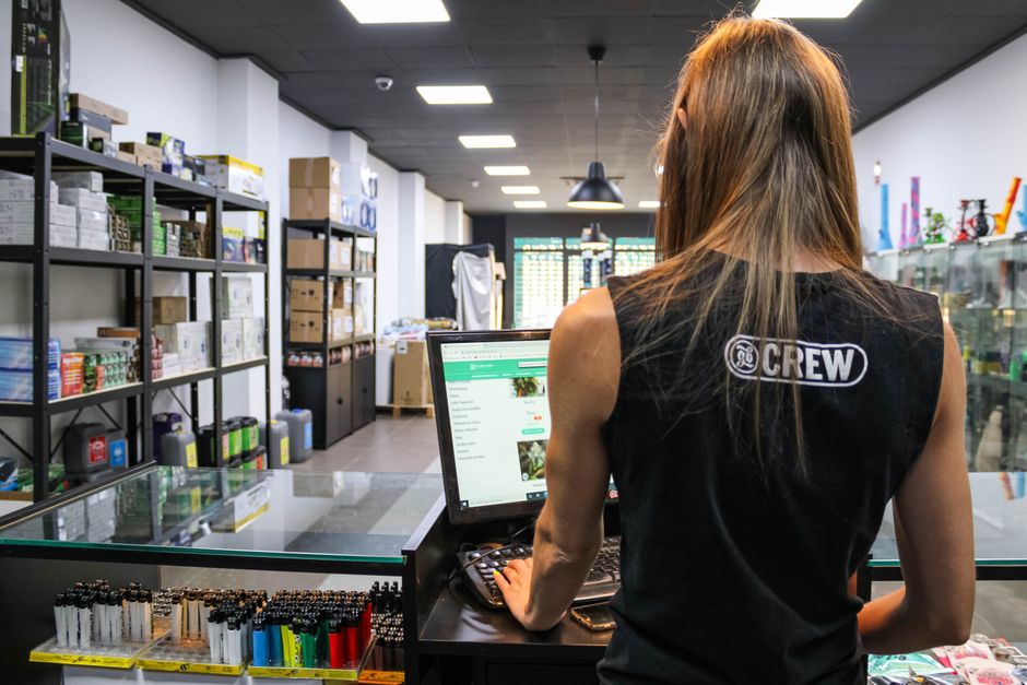 A retail worker interacts with a computer at a store counter filled with various goods.