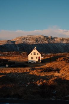 White house in the Iceland wilderness at sunset with mountain backdrop.