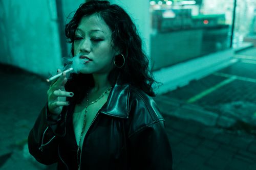 Free A woman in a leather jacket smoking a cigarette at night under neon lights. Stock Photo