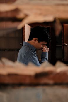 一名疲惫沮丧的黑发年轻人，穿着休闲服装，在黑暗的房间里揉眼睛的侧面图