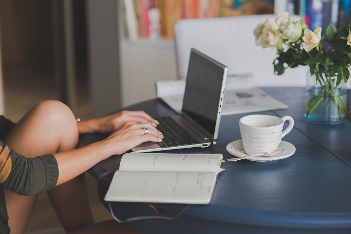 a woman sitting at a table using a laptop computer with tea and a journal