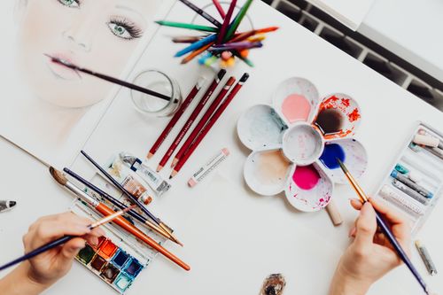 Free Flat lay of art supplies, including brushes and paint, used in creating a colorful portrait. Stock Photo