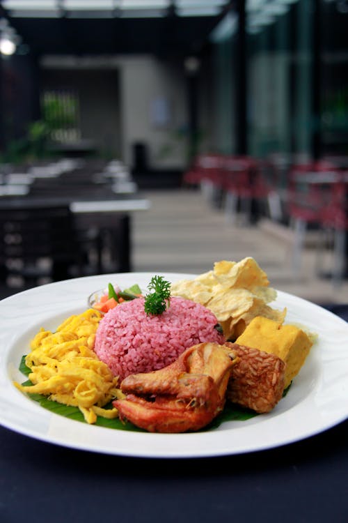 From above of delicious Nasi Ungu dish with rice served on white plate with chicken and various Asian snacks in cafe