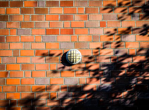 Free Sunlit red brick wall with geometric shadows and central outdoor light fixture. Stock Photo