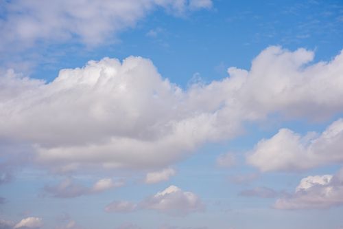 Free A serene view of fluffy cumulus clouds against a clear and vibrant blue sky. Stock Photo