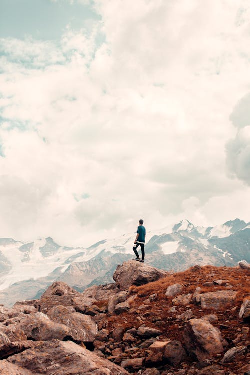 Unrecognizable hiker standing on edge of mountain and admiring view of mountain range under  cloudy sky