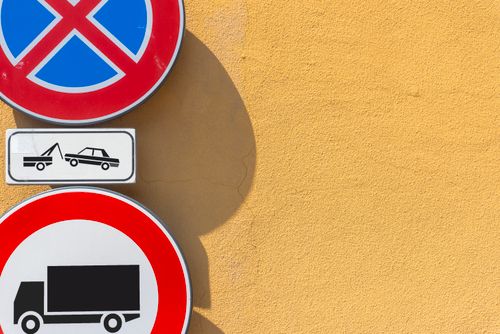 Free Traffic signs against a bright yellow wall; no parking and truck prohibition displayed. Stock Photo