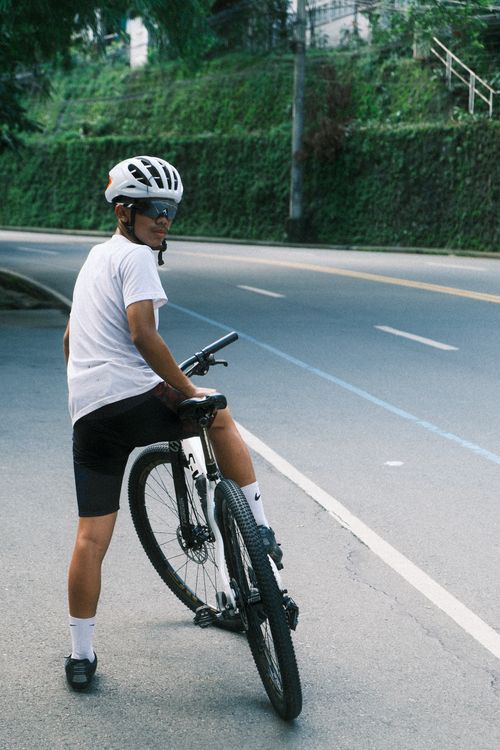 Free A cyclist pauses on their bike along a leafy, curved road during daytime. Stock Photo
