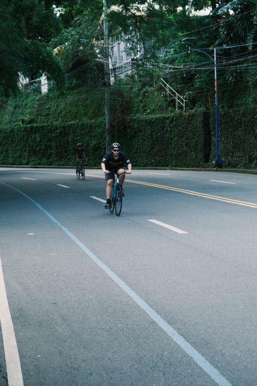 Free Cyclist enjoying a peaceful ride along a tree-lined road in daylight, embracing nature. Stock Photo