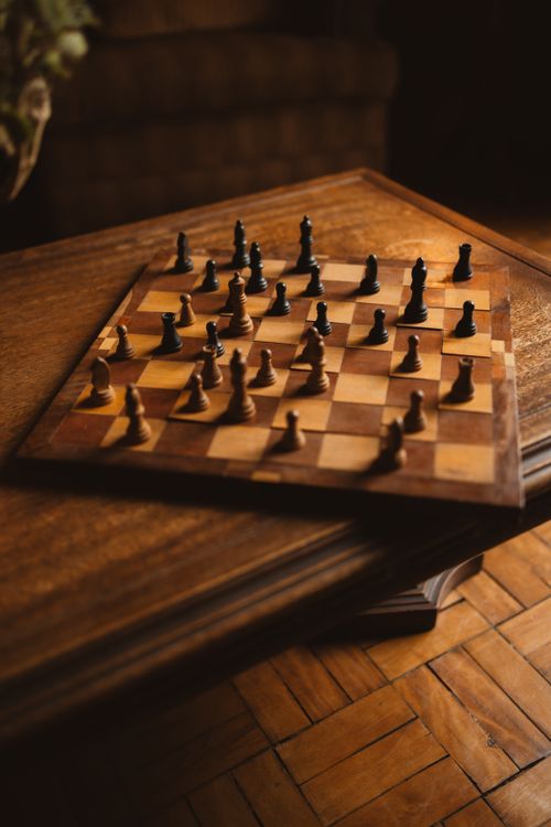Free Overhead view of a chess game in progress on a wooden board with warm lighting, creating a classic mood. Stock Photo