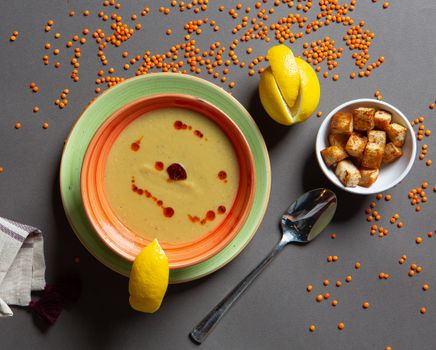 A warm bowl of red lentil soup served with lemon wedges and croutons, styled as a flat lay.