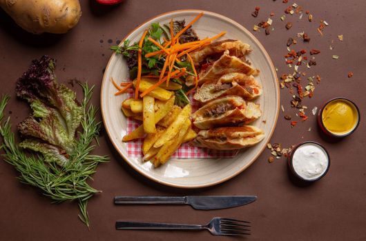Delicious gourmet sandwich with fries, salad, and sauces on a brown table setting.