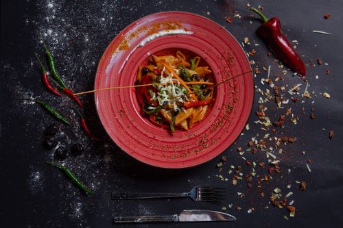 Free Top view of spicy pasta dish with vibrant peppers served on a red plate. Stock Photo