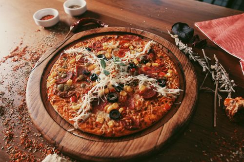 Free Top-down view of pepperoni pizza with olives, corn, and spices on a wooden board. Stock Photo