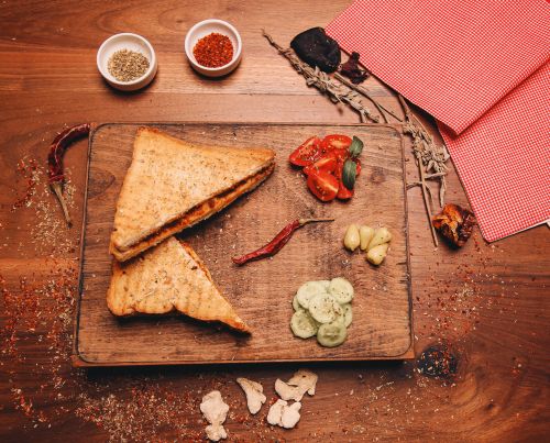 Free Delicious grilled sandwich served with fresh tomatoes, cucumbers, and spices on a wooden board. Stock Photo
