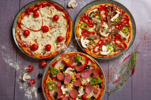 Free Top-down view of three gourmet pizzas with various toppings on a rustic wooden table. Stock Photo