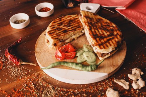 Free Mouth-watering grilled panini sandwich served with fresh tomatoes and cucumbers on a wooden board. Stock Photo