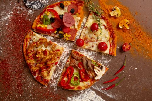 Free Overhead view of various pizza slices with fresh ingredients and spices on a table. Stock Photo