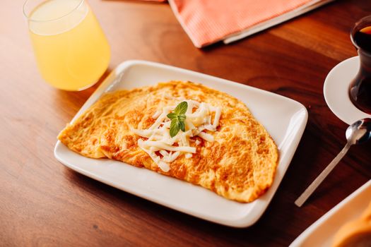 A warm cheese omelette garnished with herbs, served with juice and coffee.