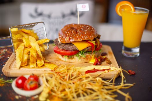 Tasty cheeseburger with crispy fries and fresh orange juice on a wooden board.