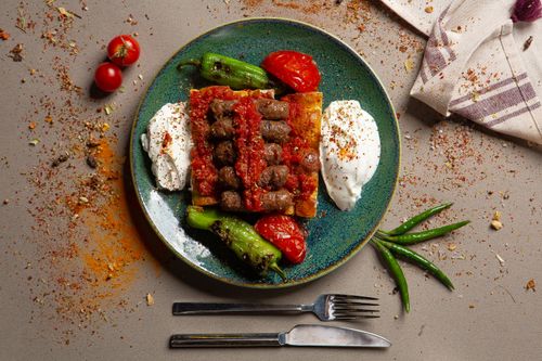 Free A beautifully plated Turkish kebab dish with yogurt, grilled peppers, and tomatoes on a vibrant ceramic plate. Stock Photo