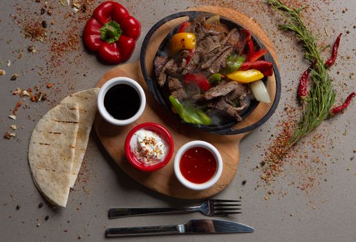 Top view of sizzling beef fajitas with colorful peppers and sauces on a wooden board.