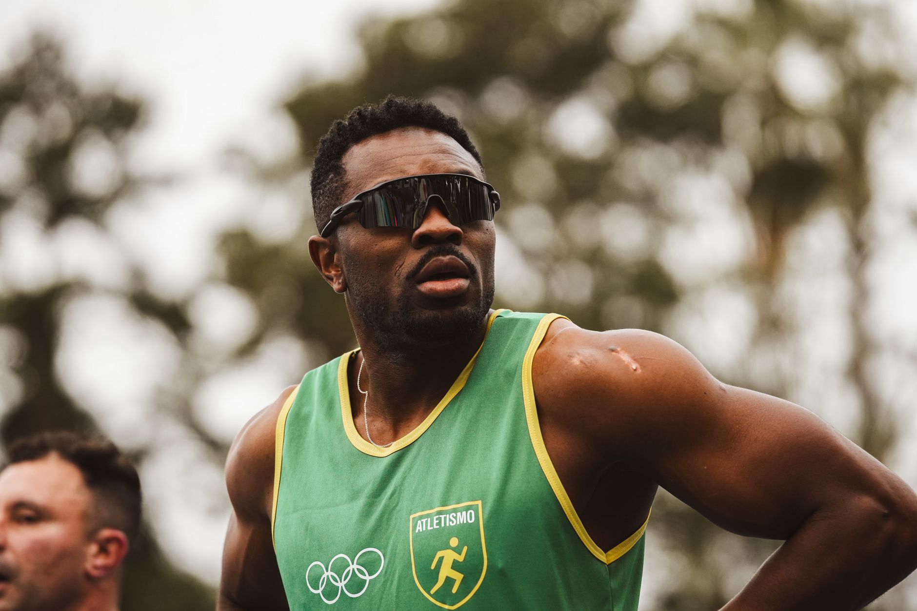 Athlete in green uniform and sunglasses getting ready for a race outdoors.