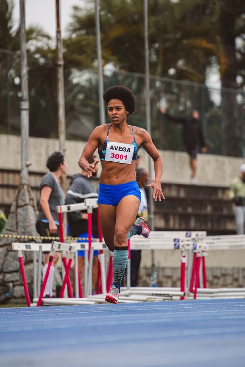 Free Focused female athlete in blue sportswear competing in a hurdle race on a track. Stock Photo