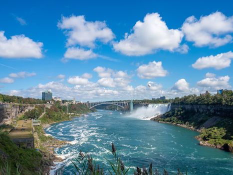 A breathtaking view of Niagara Falls with the Rainbow Bridge under a bright blue sky.