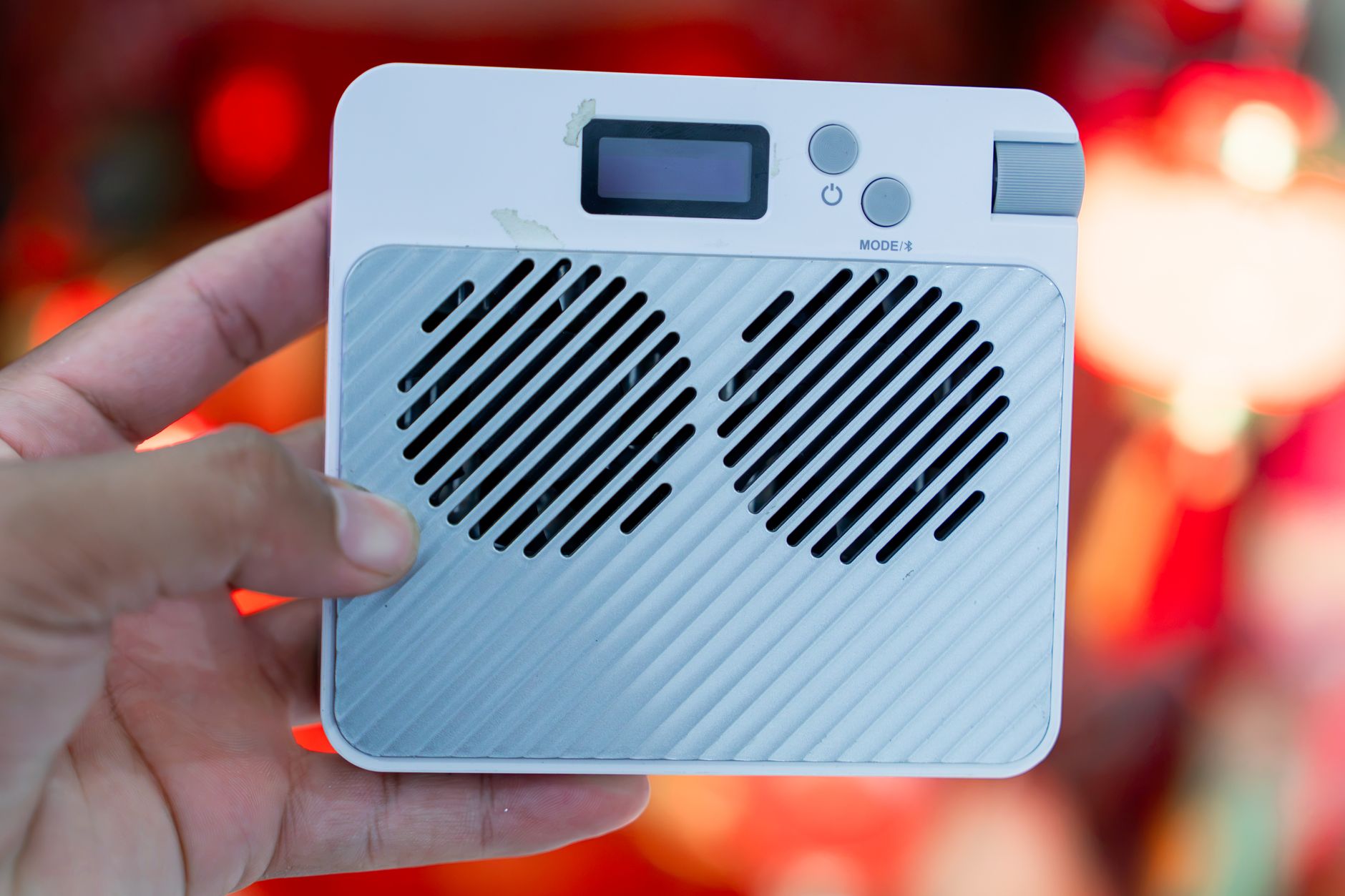 Close-up of a white portable speaker with retro design, held in hand against a colorful background.